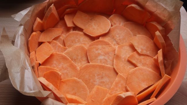 Zoete aardappel schijfjes in bakvorm om een glutenvrije quiche van te maken. 