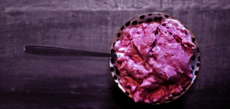 Kommetje met donkerroze nicecream (gezond blenderijs) op een donkere houten ondergrond