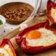 Gevulde paprika met ei - 3 halve rode paprika's met spiegelei erin - op houten plank gepresenteerd